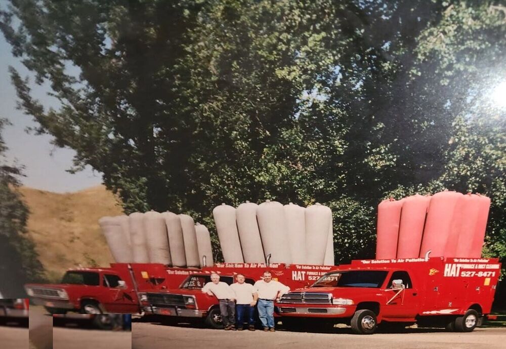 Old photograph of the original Hat Furnace & Duct Cleaning fleet: three red vacuum trucks with filter bags raised and the crew standing between them