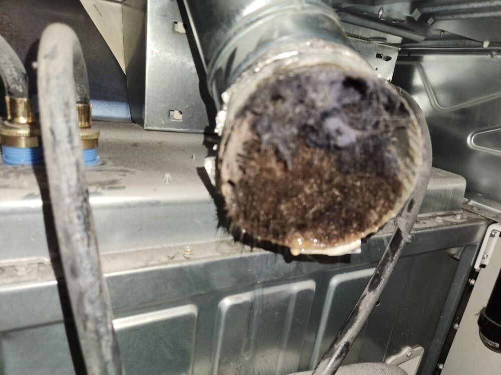 End of a vent pipe packed completely solid with grey lint and dust