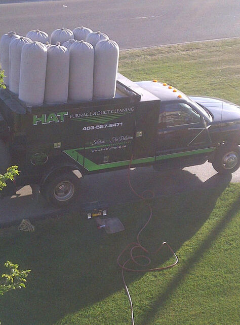 Black vacuum truck parked at a customer's home with filter bags on top and hoses across the lawn