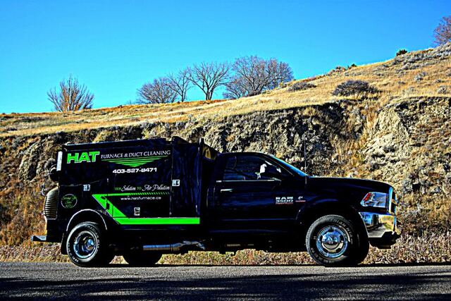 The black HAT vacuum truck parked on a road below a prairie hillside
