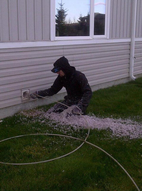 Technician clearing built-up debris out of an exterior wall vent onto the lawn