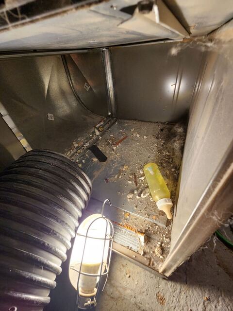 Inside a home's ductwork mid-clean, with a work light, vacuum hose and an old baby bottle found in the duct