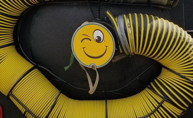 Winking smiley-face cap on the truck's vacuum inlet surrounded by coiled hoses