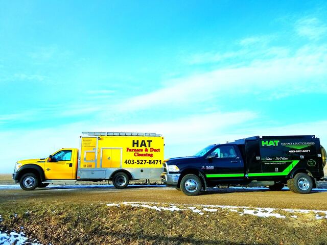 The yellow and black HAT vacuum trucks parked nose to nose on a prairie road under a bright blue sky