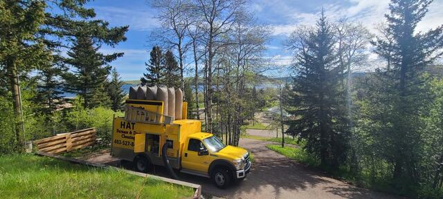 The yellow truck working at a property in the trees with a lake and hills in the distance